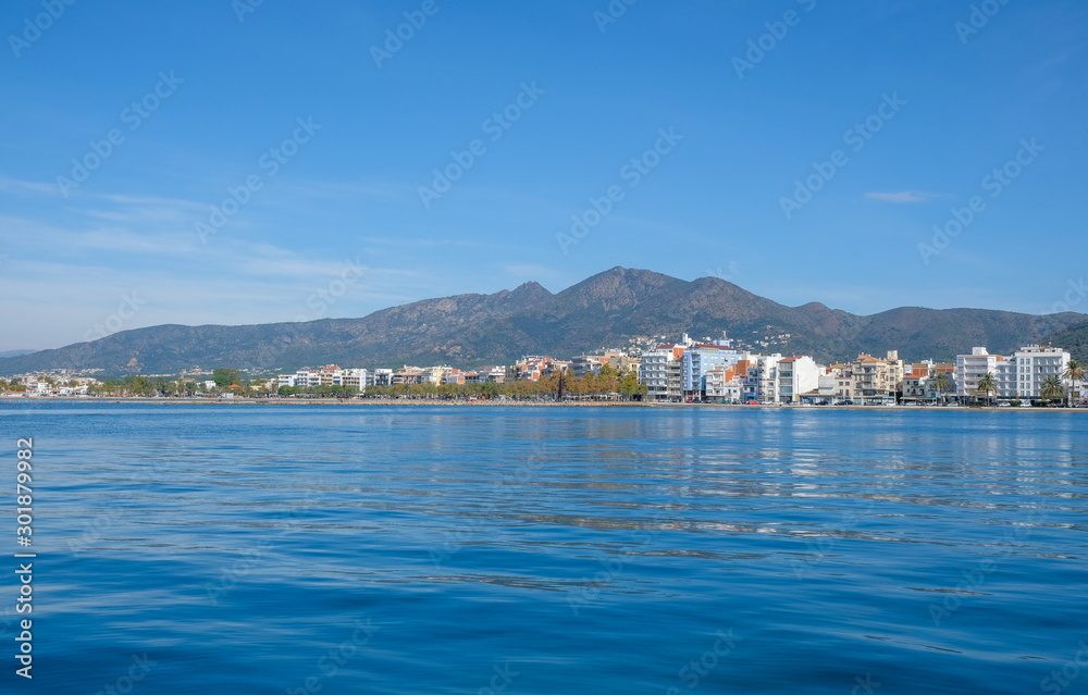 Seascape in Roses, Catalonia, Spain. City on the mountain on the coast on blue sky background. Beautiful panoramic view in the sunny day, natural background. The bay and the city.
