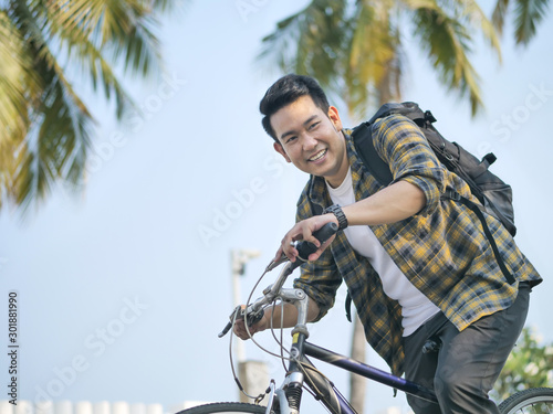 Happy Asian man with backpack riding bicycle with green tree