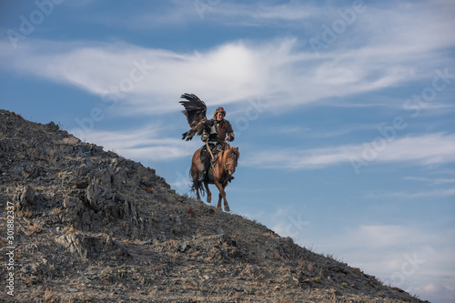 Eagle hunter descending from a hill with his eagle and horse. © Kertu
