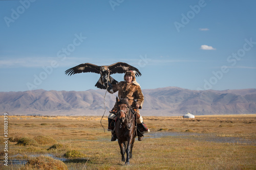 Canvastavla A proud young kazakh eagle hunter posing with his golden eagle on horseback on the backdrop of blue sky