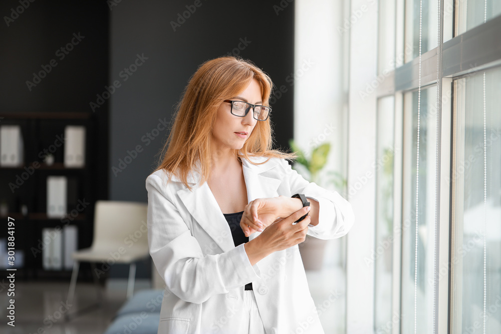 Portrait of mature businesswoman looking at watch near window in office Portrait of mature businesswoman looking at watch near window in office