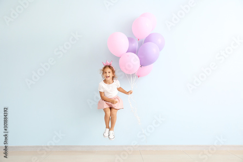 Jumping little girl with balloons on color background