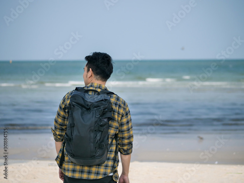 Happy Asian man wih backpack standing at the beach.