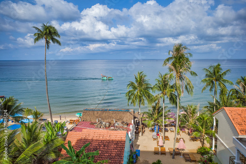 Obraz na płótnie Phu Quoc island, Vietnam - March 30, 2019: structures on the coastline on the shore of the Indian Ocean, high palm trees, boat on the water w salonie