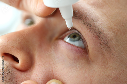 Obraz na plátně Man putting liquid drops in his eye solving vision problem