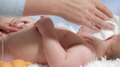 Mom wipes baby's chest with wet wipe. Child lies on white blanket on blue background, mother wipes his chest with wet cloth. Slow motion photo