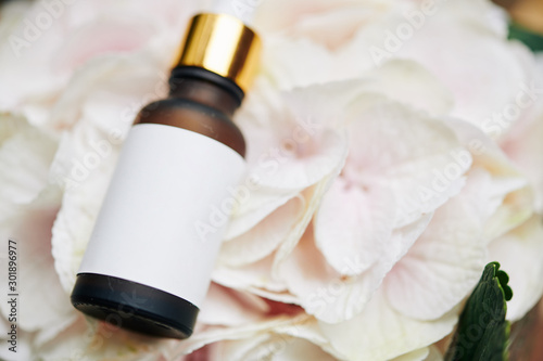 Small glass bottle of essential oil on light pink flower petals  selective focus