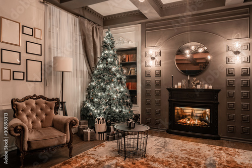 Christmas evening by candlelight. classic apartments with a fireplace, decorated tree, sofa, large windows and chandelier.