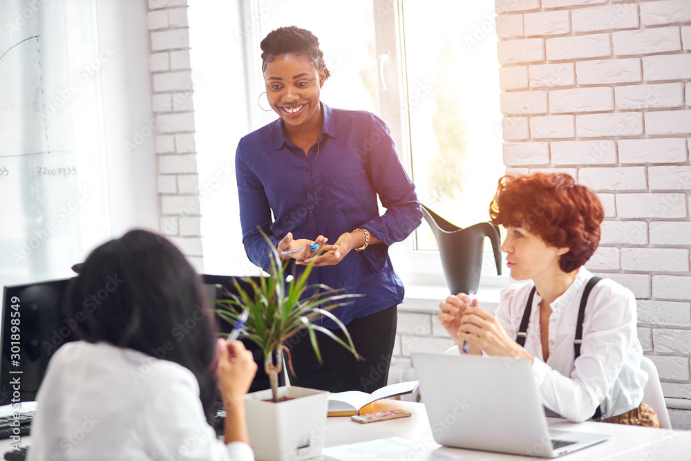 Fototapeta premium Smiling african business coach working with flipchart reporting about work result, explaining new project idea to caucasians.