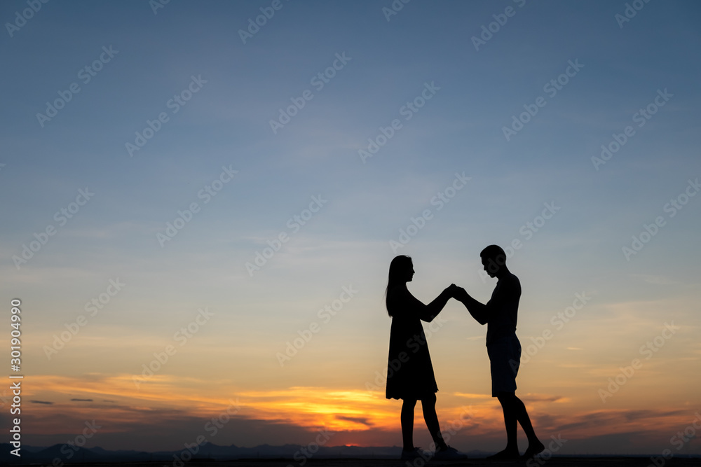 Silhouettes of happy young couple against the sunset sky.
