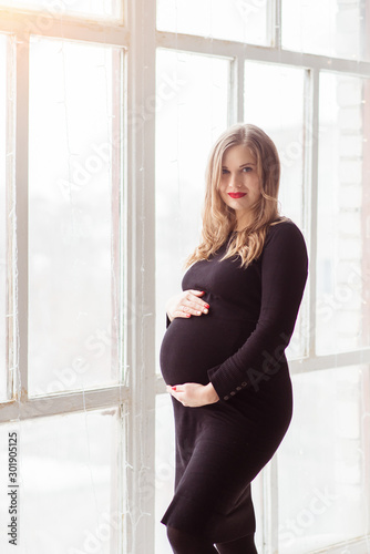 Pregnant woman standing in a black dress near the window