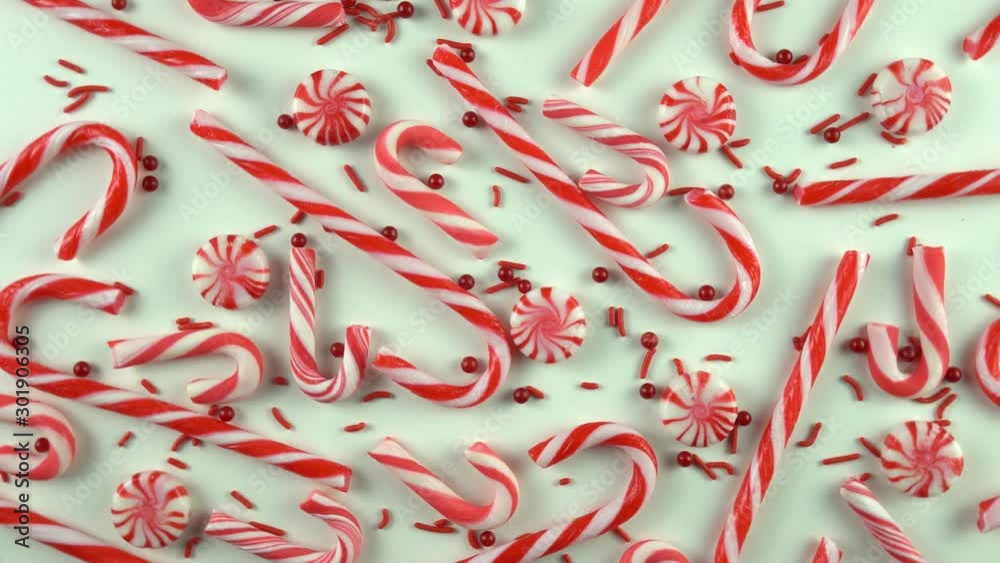 Close up of Christmas Eve season red color mood table with candy canes and peppermint spinning over white background. Holiday scene with pearls sprinkles.