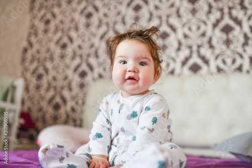 baby posing on camera sitting on the bed. The child plays in bedding.