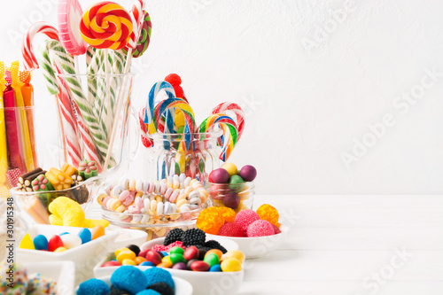 Different colorful candy sweets. Mix candy confectionery in jars on white wooden background with copy space photo