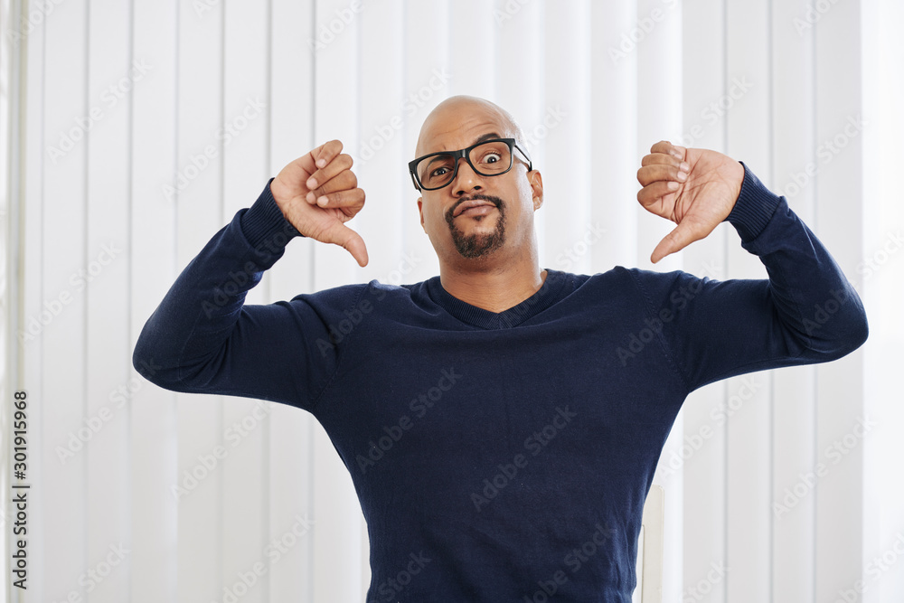 Portrait of unhappy fit man in glasses showing both thumbs-down and lookig at camera