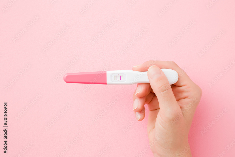 Young woman hand holding pregnancy test with two stripes on pastel pink  background. Positive result. Closeup. Point of view shot. Top down view.  Stock Photo | Adobe Stock