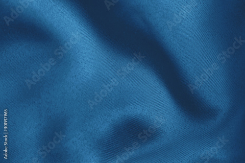 Dark blue colored Background of soft draped fabric. Beautiful satin silk textured cloth for making clothes and curtains. Elegant textile texture. Color trend concept.