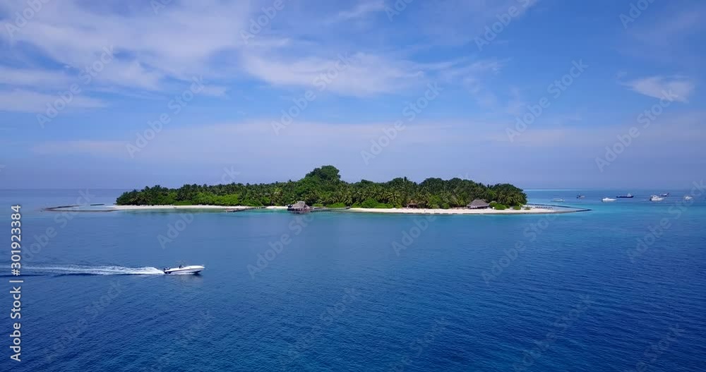 Motor boat sailing around exotic island across deep blue sea water on a beautiful day with light blue sky in Maldives