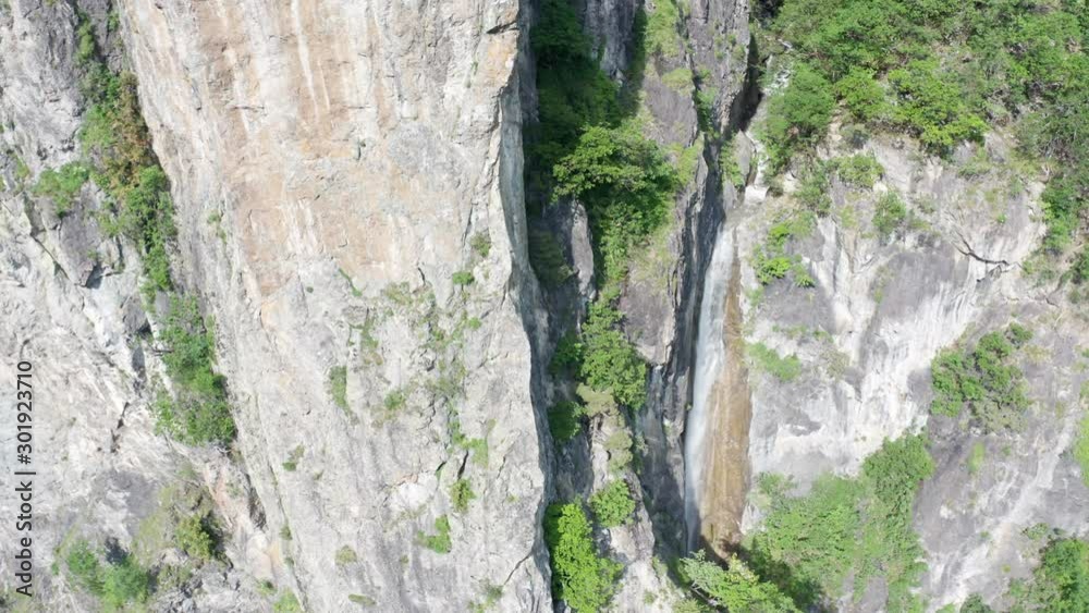 Aerial of large cliff with a waterfall running next to it Aerial of large cliff with a waterfall running next to it