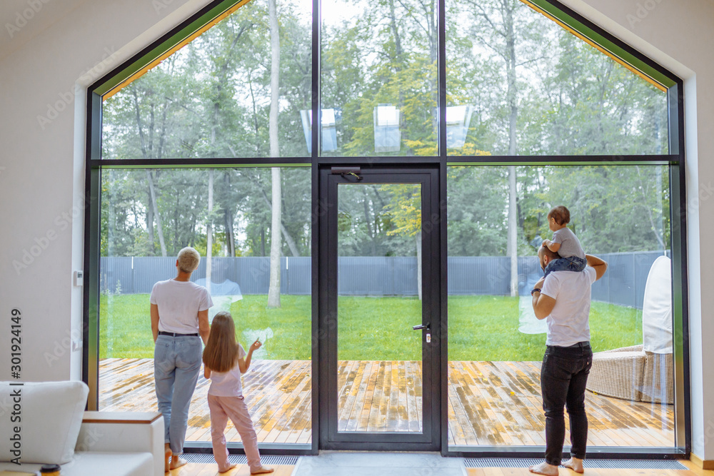 Back of Parents with children look at panoramic window together, relaxing together, spending time at home. Modern house interior Back of Parents with children look at panoramic window together, relaxing together, spending time at home. Modern house interior