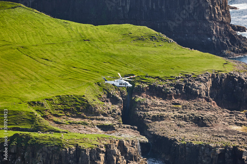 Helicopter flying over mykines atlantic cliffs in Faroe. Denmark photo