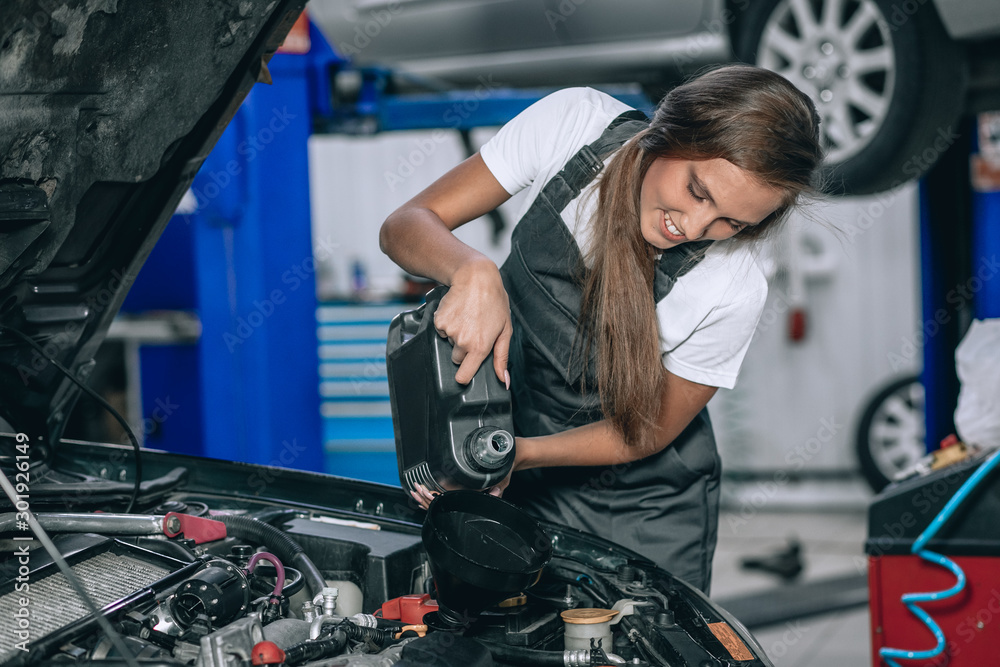 Beautiful Mechanic  girl in a black jumpsuit and a white T-shirt changes the oil in a black car. car repair concept