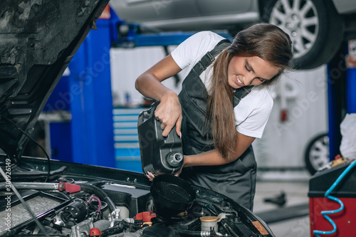 Beautiful Mechanic  girl in a black jumpsuit and a white T-shirt changes the oil in a black car. car repair concept © Semachkovsky 