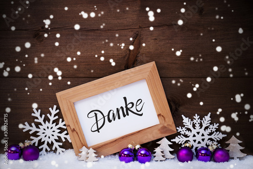Frame With German Calligraphy Danke Means Thank You. Pruple Christmas Ornament Like Ball, Tree And Star. Wooden Background With Snow