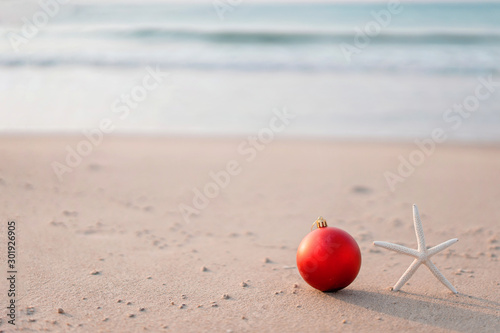 Christmas ball and starfish on yellow sand and sea background. New Yeaar or Xmas holiday vacation in exotic countries or tropics concept: christmas decorations on the beach. Copy space for text