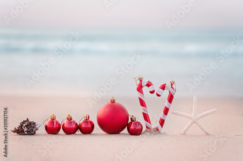 Christmas ball and starfish on yellow sand and sea background. New Yeaar or Xmas holiday vacation in exotic countries or tropics concept: christmas decorations on the beach. Copy space for text