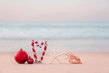 Christmas ball and starfish on yellow sand and sea background. New Yeaar or Xmas holiday vacation in exotic countries or tropics concept: christmas decorations on the beach. Copy space for text