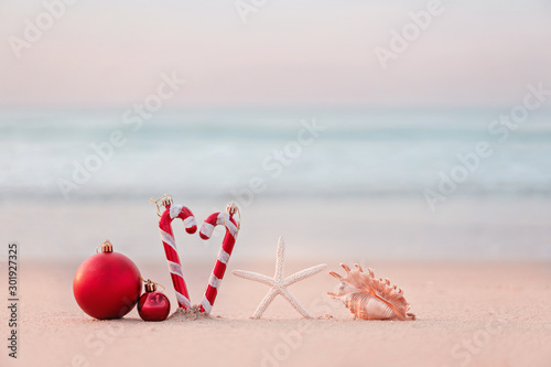 Fototapeta Naklejka Na Ścianę i Meble -  Christmas ball and starfish on yellow sand and sea background. New Yeaar or Xmas holiday vacation in exotic countries or tropics concept: christmas decorations on the beach. Copy space for text