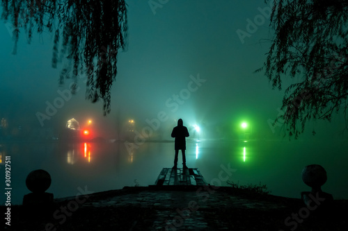 silhouette of a man and a lake in the fog at night