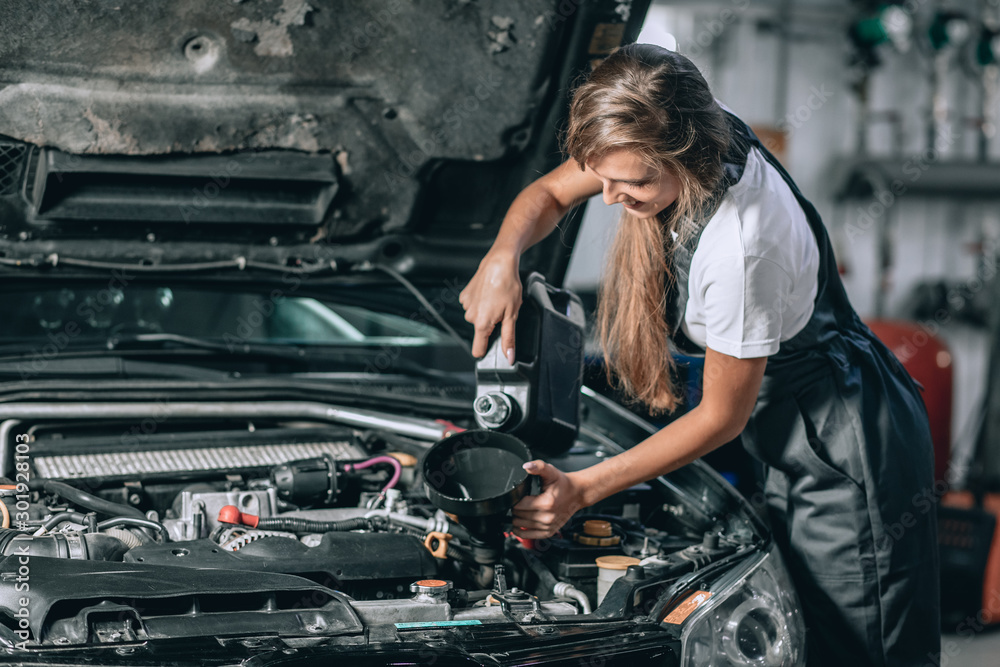 Beautiful Mechanic girl in a black jumpsuit and a white T-shirt changes the oil in a black car. car repair concept Beautiful Mechanic girl in a black jumpsuit and a white T-shirt changes the oil in a black car. car repair concept