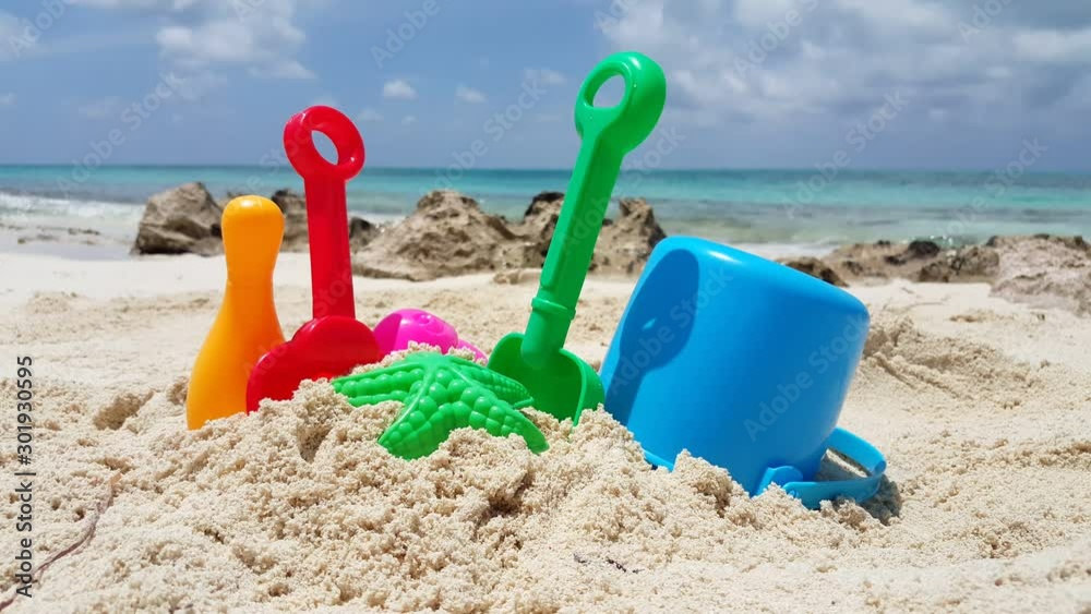 Beach toys on vivid colors leftover on white beach of tropical island with sky and ocean background, copy space Beach toys on vivid colors leftover on white beach of tropical island with sky and ocean background, copy space