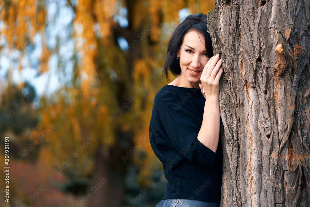 Beautiful elegant woman standing and posing near tree in a city park in autumn Beautiful elegant woman standing and posing near tree in a city park in autumn