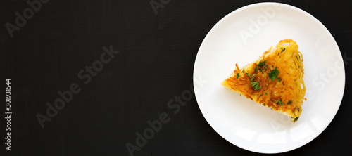 Homemade spaghetti omelette on a white plate over black background, top view. Flat lay, overhead, from above. Space for text.