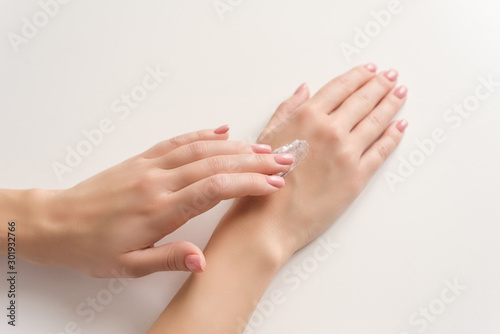 Hands of a girl with a Nude manicure on a light background moisturize the skin with a white cream. Beautiful young woman hands with cream  isolated on white. The concept of fashion  moisturizing