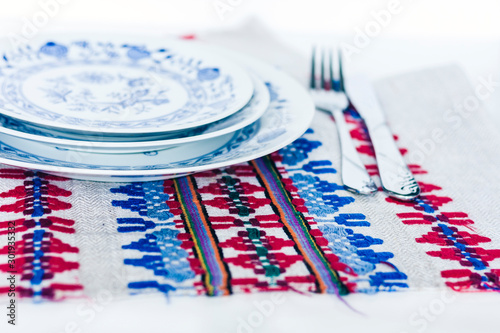 Table setting for dinner: a white plate, a fork, a knife on a woven cloth napkin with an embroidered pattern,  traditional handmade in Ukraine.