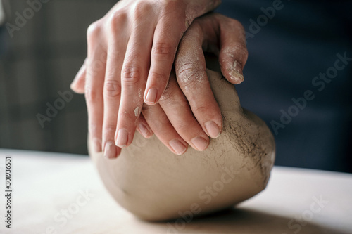 Female potter hands working with clay in workshop. White desk on background