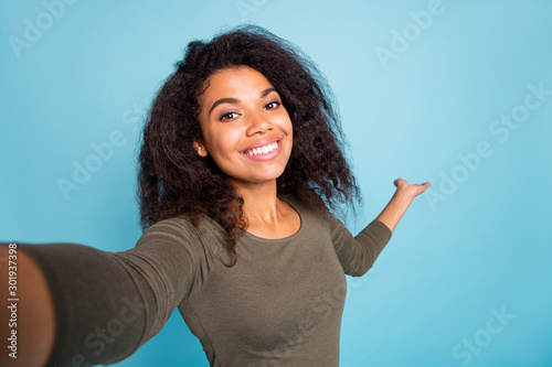 Close up photo of positive cheerful afro american tourist girl hold hand invite show her vacation take selfie video call wear casual style shirt isolated over blue color background