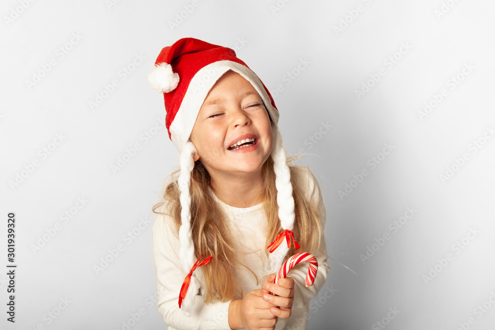 Portrait of little pretty girl laughs in Santa hat with lollipop candy isolated on white background. Happy Christmas holidays, cute child in happiness. Portrait of little pretty girl laughs in Santa hat with lollipop candy isolated on white background. Happy Christmas holidays, cute child in happiness.