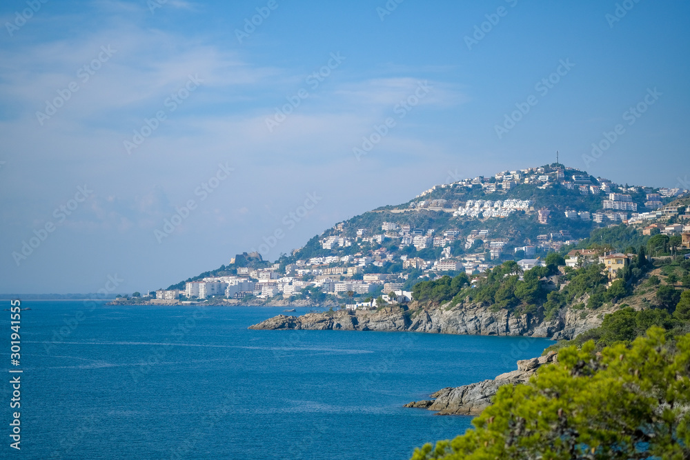 View of the city of Roses and the bay on a bright sunny day from the surrounding mountains. Vacation on the sea, hiking, active healthy lifestyle. Catalonia, Spain.