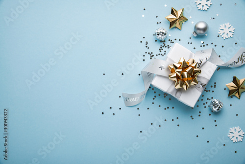 Merry Christmas and Happy Holidays greeting card, frame, banner. New Year. Noel. Christmas white and golden ornaments and gifts on blue background top view. Winter xmas holiday theme. Flat lay.
