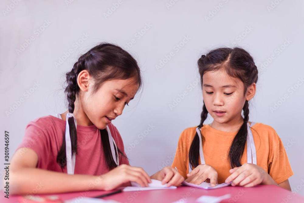 Two cute Asian elementary girls are teaching origami. Two cute Asian elementary girls are teaching origami.