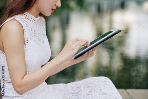 Cropped image of young woman working on digital tablet when sitting at small pond in city park