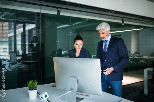 Two businesspeople with computer in an office standing at desk.