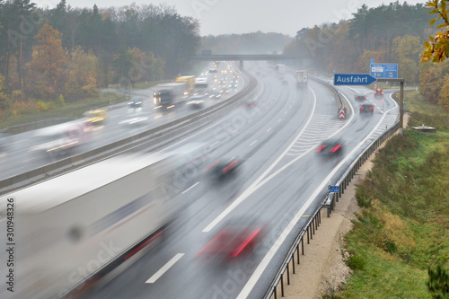 The highway A3 near the exit " Nürnberg Nord " (in English: Nuremberg North ) with many cars with lights switched on driving with speed on a wet rainy day in November with autumn forest around
