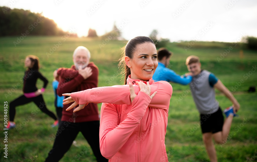Large group of fit and active people stretching after doing exercise in nature. - obrazy, fototapety, plakaty 