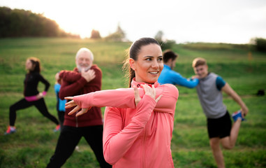 Large group of fit and active people stretching after doing exercise in nature.